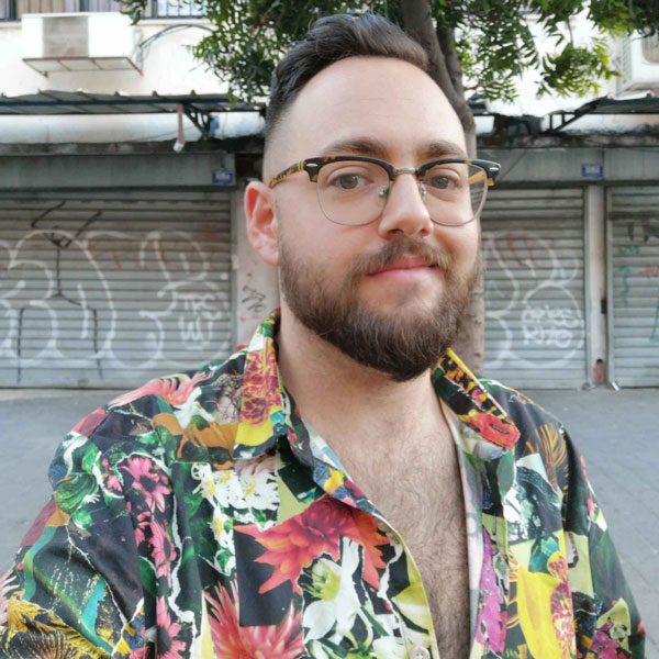 a man with a beard and glasses standing in front of a building