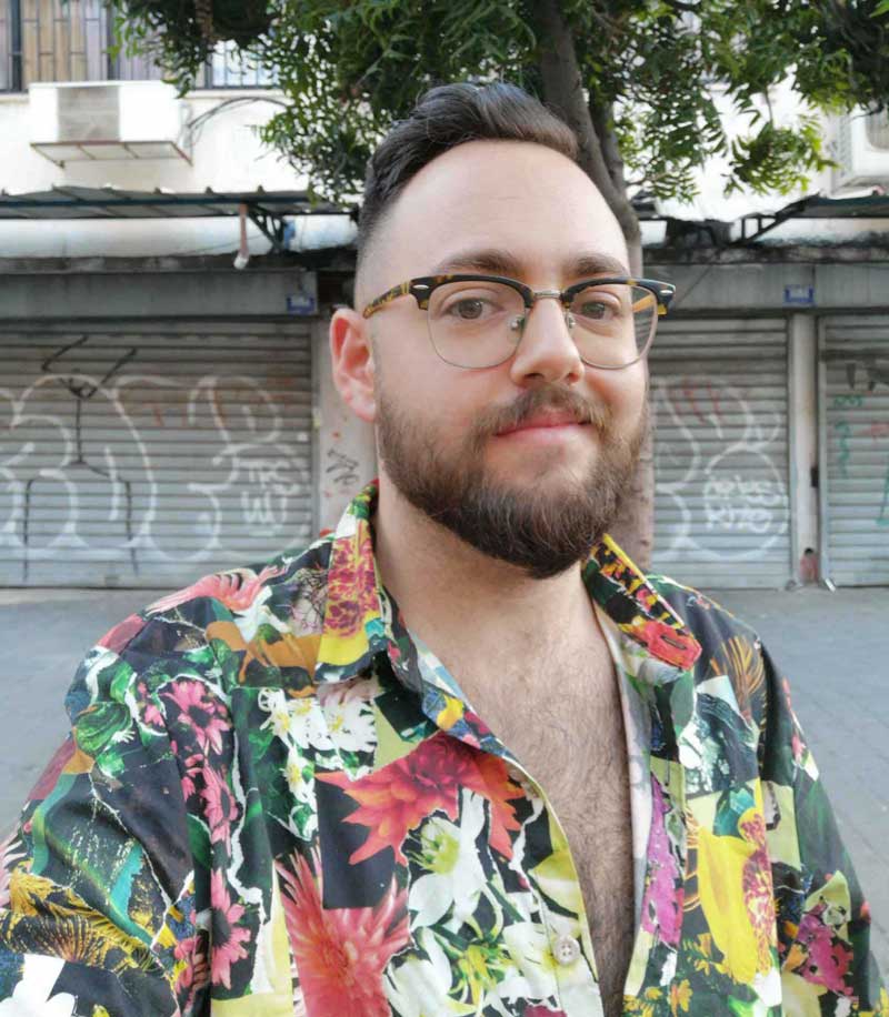 a man with a beard and glasses standing in front of a tree